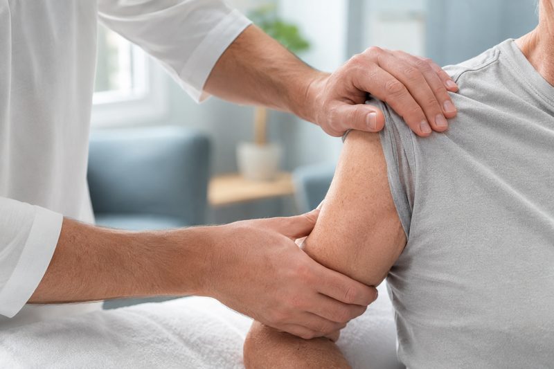 Hände des Physiotherapeuten bei einer manuellen Behandlung an der Schulter